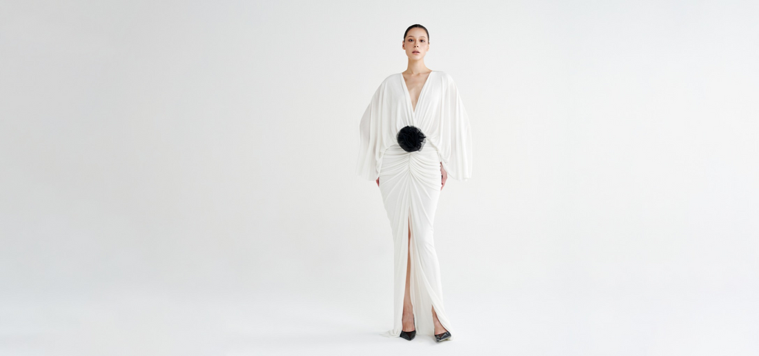 Model in the white Rosette Plunging Batwing Ruched Dress, with a black rosette at the waist and a split maxi hem