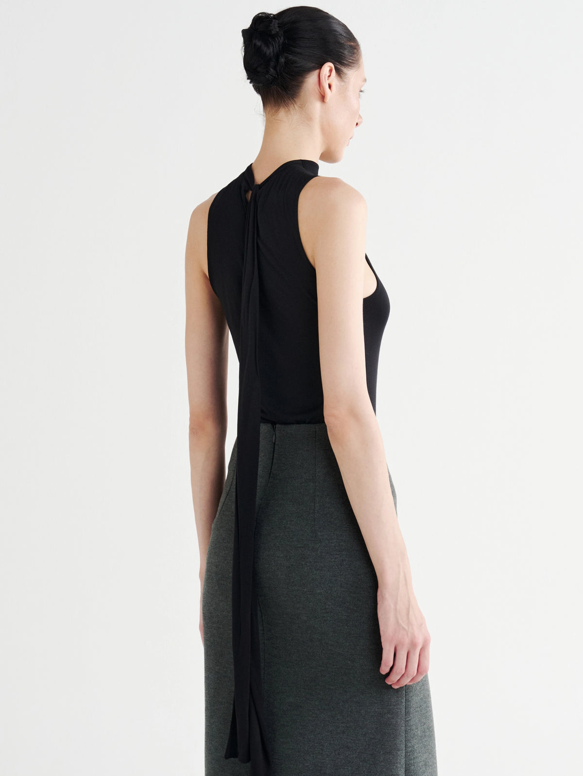 Back view of the black Back-Tie Mock Neck Tank, its tie down the spine, with the gray Minimalist Column Skirt